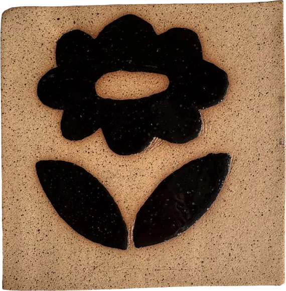 Square stoneware tile in speckled tan clay with a bold black flower and two leaves in relief.